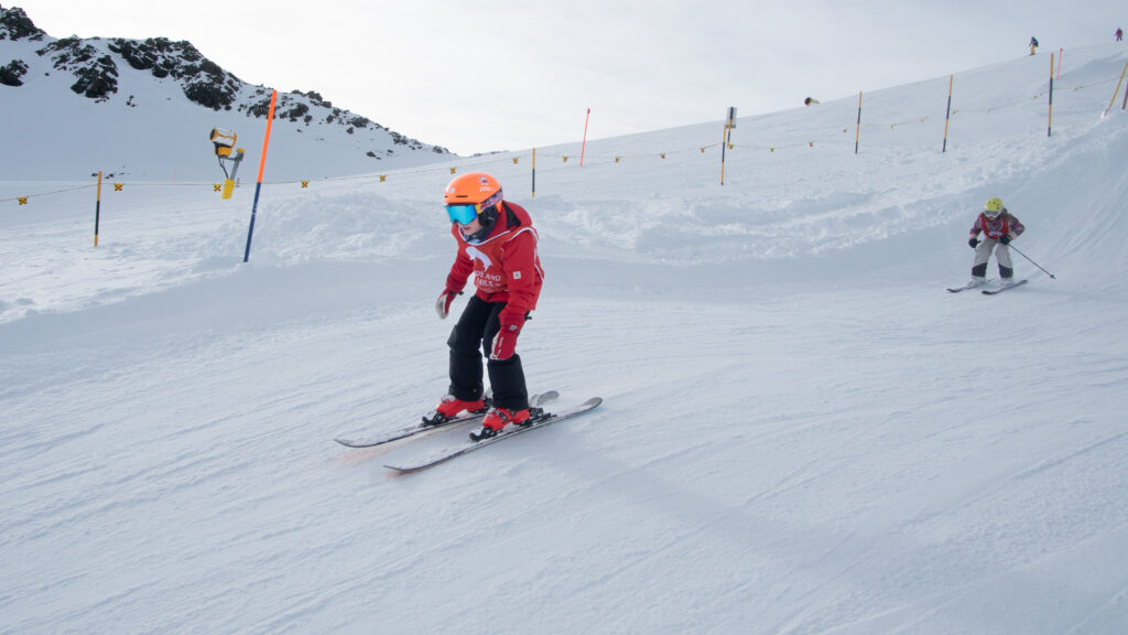 Two children skiing downhill wearing marked vests from the Davos Ski School